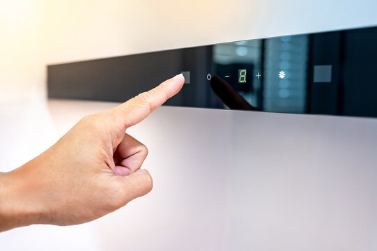 Hand touching digital switch panel on modern black kitchen hood to operate extractor fan and light. Adjusting mode of cooker hood. Home appliance in the kitchen