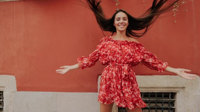 Female subject outdoors shows playful expressions, relaxed arms, heart hands, hair touch and lively jump beside textured terracotta wall, with warm daylight, vivid pattern and clean negative space