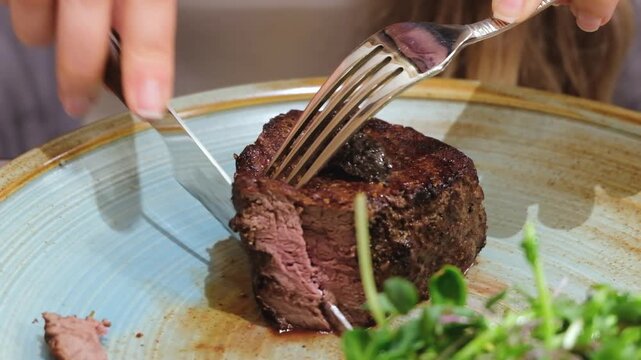 Woman cutting juicy medium rare fillet mignon steak with knife and fork on restaurant plate for dining.