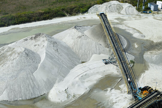 Aerial view of a gravel pit with large piles of sand and gravel, a conveyor belt system, and water pools in Krakow, Lesser Poland Voivodeship, Poland.