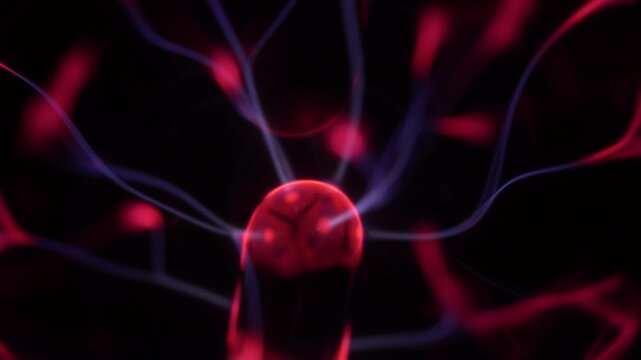 Close-up of a plasma ball coil. The plasma ball creates beams of energy in red and purple.