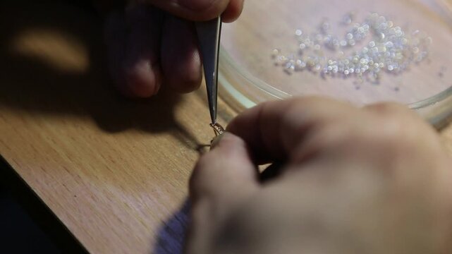 A jeweler sets gemstones into earrings. Jewelry craftsmanship. Gemstone setting.