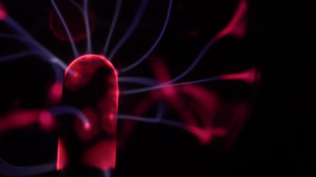 Close-up of a plasma ball coil. The plasma ball creates beams of energy in red and purple. The coil is on the left.