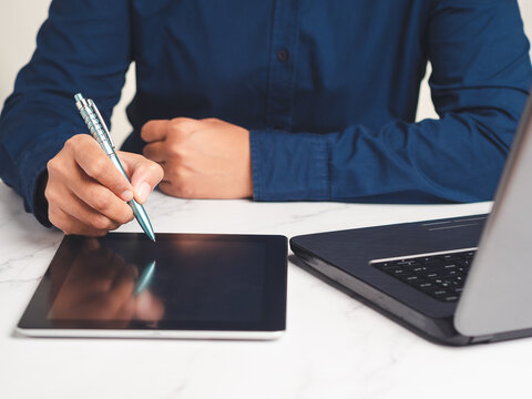 Person Writing on Tablet with Stylus Beside Laptop