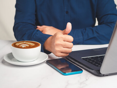 Person Giving Thumbs Up Beside Laptop and Coffee Cup