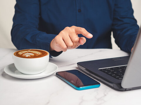 Person Pointing at Laptop Screen Beside Coffee Cup