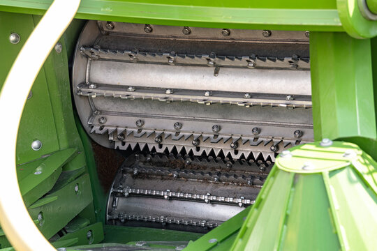 Agricultural forage harvester chopping drum with knives closeup. Modern farm crop cutting machinery component on green frame with feed rolls mechanism and engineering technical vehicle details.