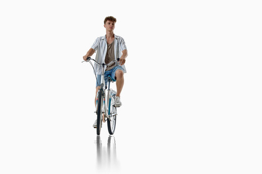 Young man rides bicycle toward camera isolated on white background. Concept of accessible active transportation, everyday fitness routine, low carbon urban mobility.