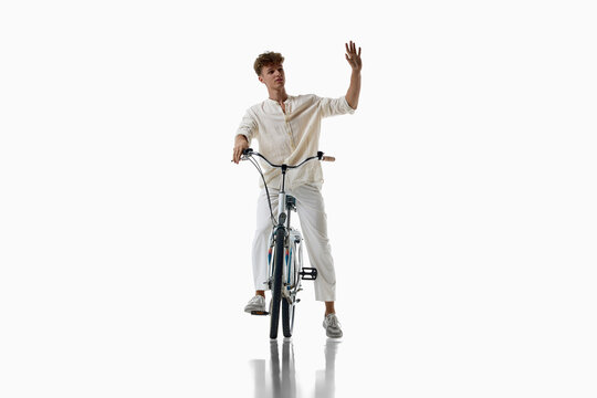 Friendly young man waves while riding bicycle toward camera. Concept of image for AI learning, positive cycling culture, welcoming social interaction, cheerful sustainable commuting.