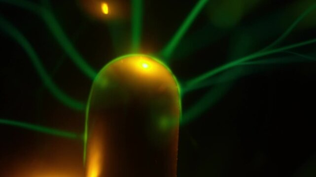 A close-up of the working coil of a plasma ball, which creates green electrical discharges. A warm beam of light illuminates the interior of the plasma ball.