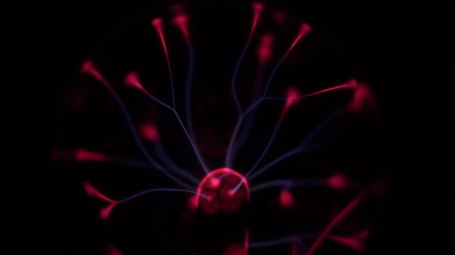 Close-up of a working plasma ball. The plasma ball's coil creates red and violet electric rays.
