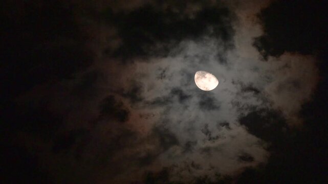 Mysterious Full Moon Partially Hidden Behind Dark Dramatic Storm Clouds at Night, Spooky Halloween Night Sky with Glowing Moonlight, Eerie Gothic Atmosphere