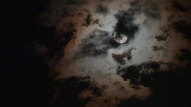 Mysterious Full Moon Partially Hidden Behind Dark Dramatic Storm Clouds at Night, Spooky Halloween Night Sky with Glowing Moonlight, Eerie Gothic Atmosphere