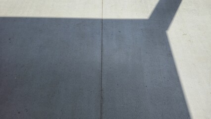Fototapeta premium Smooth concrete floor with sharp sunlight and line shadows. High-angle view of a grey cement ground with dramatic morning sun rays and architectural shadows.
