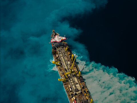 Aerial view of a large industrial vessel navigating through vibrant turquoise waters, creating a prominent white wake in the ocean, Dhidhdhoo, Thiladhunmathee Uthur, Maldives.