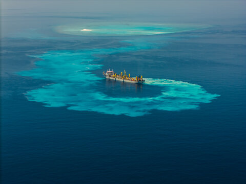 Aerial view of a large dredging ship operating in turquoise waters, creating a sediment plume while surrounded by deep blue sea near Dhidhdhoo, Thiladhunmathee Uthur, Maldives.