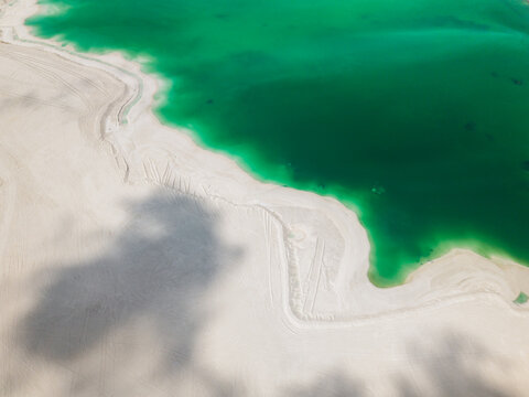 Aerial view of a vibrant turquoise lagoon meeting a pristine white sandy shore with visible tire tracks and soft cloud shadows in Dhidhdhoo, Thiladhunmathee Uthur, Maldives.