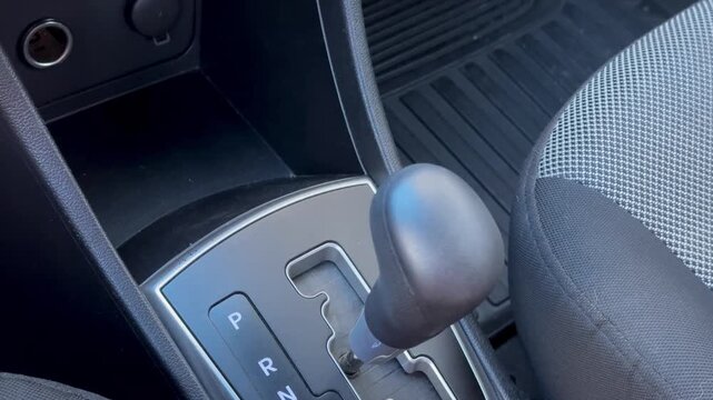 Woman hand holding automatic gear shift lever inside car, close-up of transmission selector on center console, vehicle interior, driving, transport.