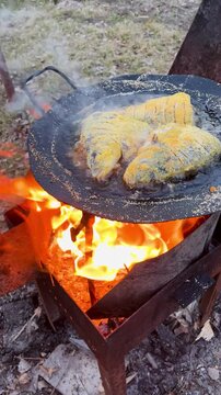 Golden cornmeal fried fish pieces sizzling over an open fire griddle