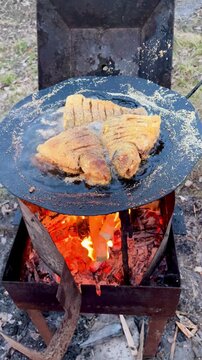 Close up of golden cornmeal fried fish pieces sizzling over an open fire griddle