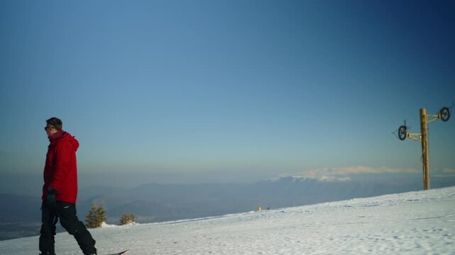 A man wearing a red jacket gracefully snowboards down a pristine snowy mountain slope. He enjoys the thrilling winter sport amidst the clear blue sky and picturesque mountain landscape.