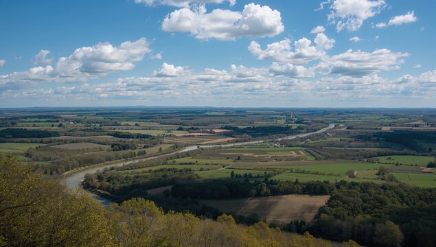 Expansive Landscape View with River and Rolling Fields Under a Blue Sky with Clouds