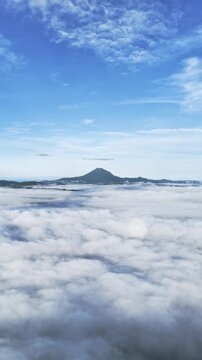 Stunning aerial view of mountain peak rising above thick rolling clouds during peaceful sunrise.