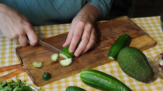 Food prep. Female hands slicing cucumber for salad on wooden board. 