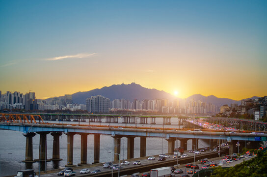 SEOUL SOUTH KOREA - November 22, 2025: Road traffic with bridge railway transport over the han river and city town landscape on golden sky cuold clear before sunset