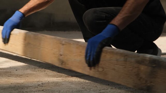 Construction worker uses a screed board to level the final sand layer before paving stone installation. Ground preparation for sidewalks, municipal infrastructure and comfortable city environment.