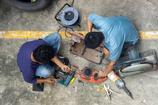 Top view of two mechanics repairing dissembled power tools on concrete floor