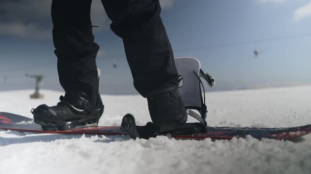 A person prepares for a ride, strapping their boots into snowboard bindings on a snowy mountain. Enjoying the winter sport, they secure their gear on a bright, cold day.