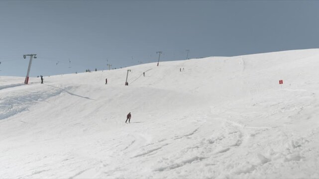 Skiers descend a pristine white slope at a busy ski resort. People are actively engaged in winter sports on a clear day.