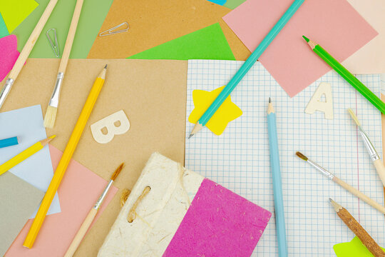 Eco-friendly school supplies on green background. Paper, wooden pencils, brushes, notebooks