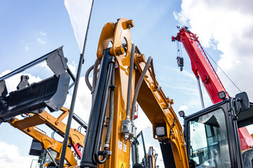 Crawler excavator boom mechanism with hydraulic lines. Modern yellow construction machinery arm cylinder linkage perspective view with red crane boom and industrial vehicle technical details. © NastyaPhoto
