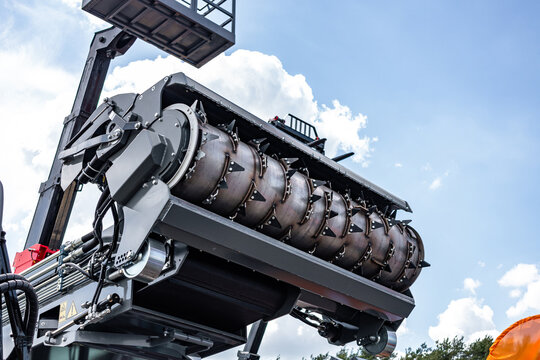 Agricultural machinery silage defacer rotor with metal teeth. Modern farm cultivation equipment cutter attachment assembly on loader boom section with industrial transport vehicle details.