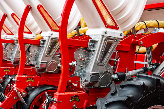 Precision seed metering unit on agricultural planter machine. Row crop seeder detail featuring aluminum distributor housing, plastic hoppers, red steel frame, and vacuum suction system.