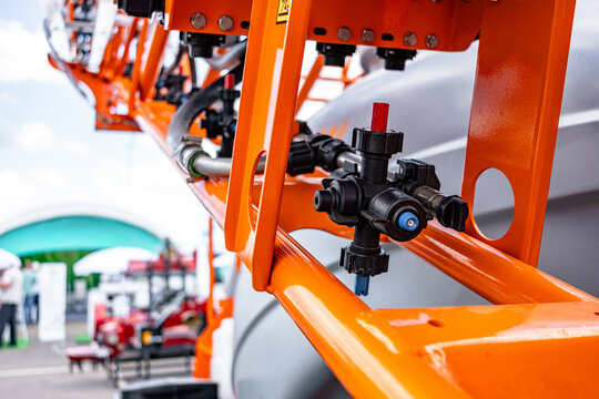 Multi nozzle turret and spray line on field boom sprayer arm. Close up detail of agricultural crop protection machinery featuring rotating tip holder, fluid line hose, and steel frame.