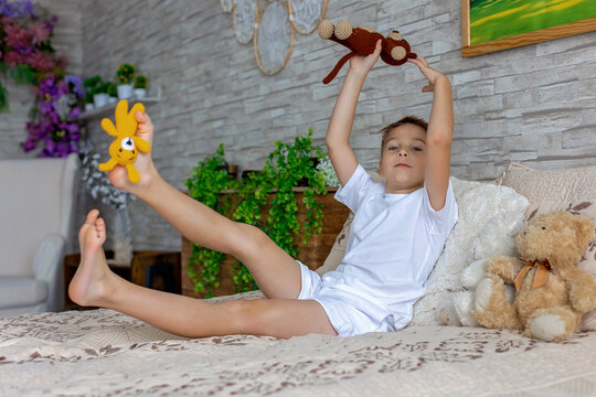 Cute little preschool child, cute blond boy, playing in bed with many teddy bears, handmade amigurumi toys, enjoying toy game