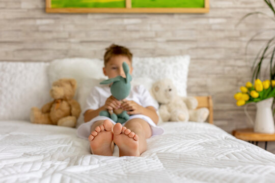 Cute little preschool child, cute blond boy, playing in bed with many teddy bears, handmade amigurumi toys, enjoying toy game
