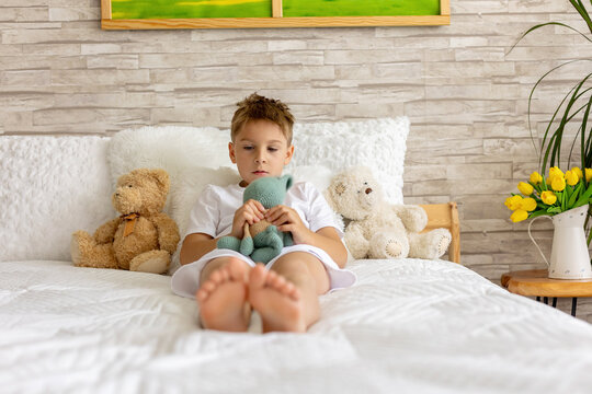 Cute little preschool child, cute blond boy, playing in bed with many teddy bears, handmade amigurumi toys, enjoying toy game