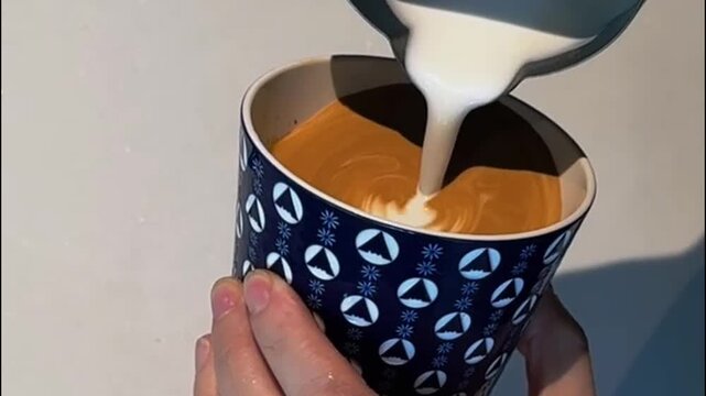 Barista pouring milk for heart rosette latte art in patterned ceramic cup