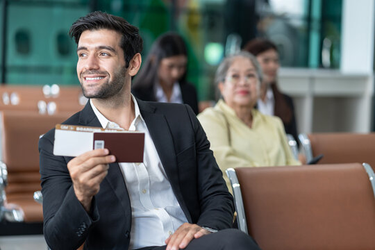 young male executive in suit holding passport with boarding pass, sitting in modern airport terminal,preparing for corporate business trip or international flight