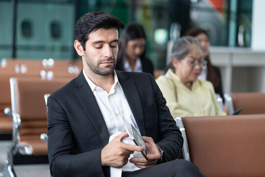young male executive in suit holding passport with boarding pass, sitting in modern airport terminal,preparing for corporate business trip or international flight