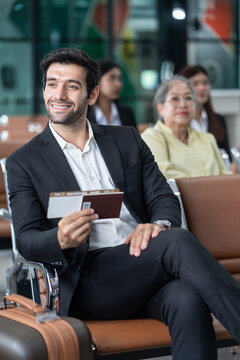 young male executive in suit holding passport with boarding pass, sitting in modern airport terminal,preparing for corporate business trip or international flight