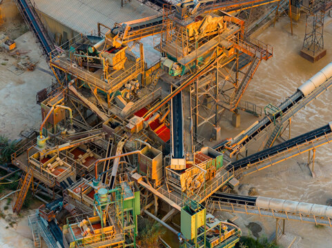 Aerial view of an industrial crushing and processing plant with conveyor belts and metal machinery set against a dusty ground in Rome, Lazio, Italy.