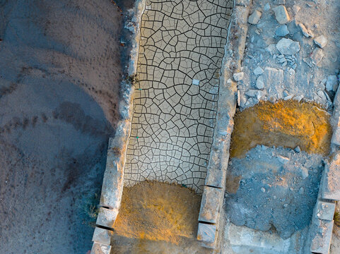 Aerial view of an industrial site featuring a cracked, dry ground surface bordered by stone walls and piles of gravel in Rome, Lazio, Italy.