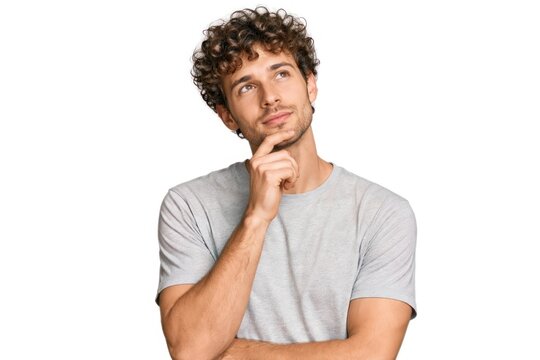 Man with curly hair in a gray shirt, pondering with hand on chin.
