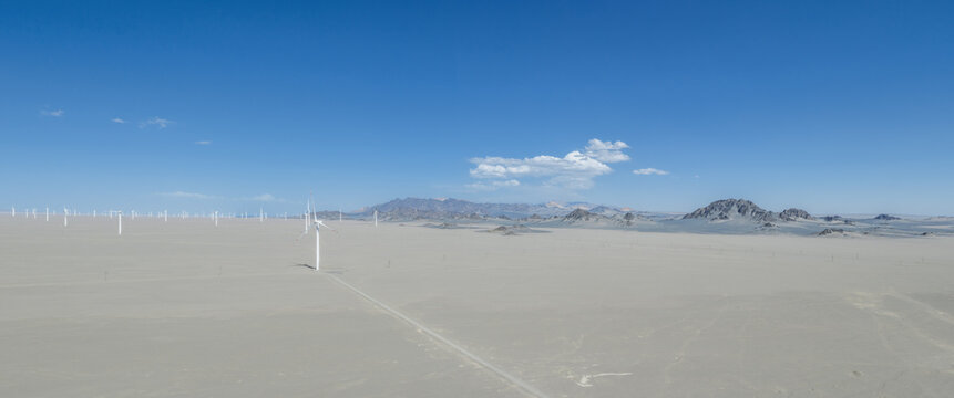 Expansive Wind Farm Array In Gobi With Desert Mountain Range Under Blue Sky