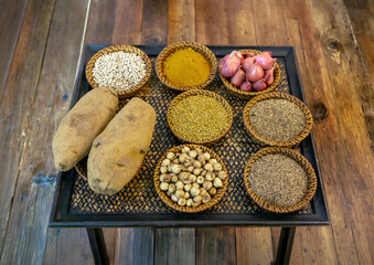 Fototapeta premium assortment of various aromatic spices, seeds, fresh shallots, and potatoes arranged in wicker bowls on a rustic wooden table for cooking preparation.